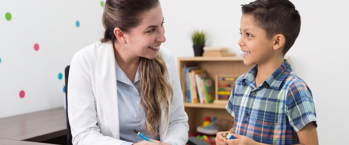 A clinician smiling with a young boy during an evaluation session, with a drawing and markers on the desk